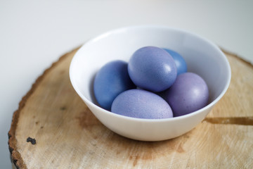 painted purple eggs in a plate on a light Easter background