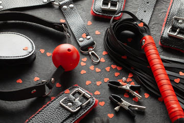 BDSM sex toys for adults. Small red hearts on black background whip, gag, handcuffs and leather...