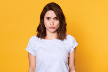 Fototapeta premium Portrait of attractive miserable girl having disappointed look on her face, looking directly at camera. Emotional charming model poses isolated over yellow background. People and emotions concept.