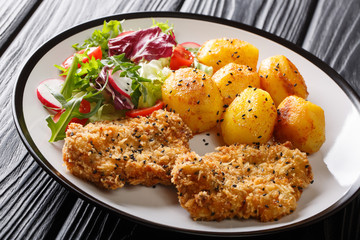 Main course fried steaks in sesame breaded with new potatoes and vegetable salad close-up on a plate. horizontal