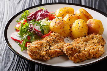 Crispy steaks in sesame breading with new potatoes and fresh salad close-up on a plate. horizontal