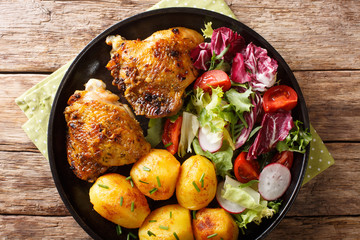 Roasted chicken thighs with new potatoes and fresh salad close-up on the plate. horizontal top view