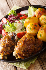 Roasted chicken thighs with new potatoes and fresh salad close-up on the plate. vertical