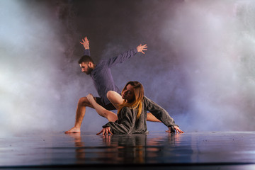 Shoeless dance couple performing multiple unique dance moves in front of a black background surrounded by a lot of smoke.