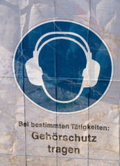 Symbol on a transparent tarpaulin as an indication of safety on a construction site. You can see that you should wear earmuffs. The text means in German: Wear earmuffs.
