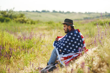 Naklejka na ściany i meble 4th of July. Fourth of July. American with the national flag. American Flag. Independence Day. Patriotic holiday. The man is wearing a hat, a backpack, a shirt and jeans. Beautiful sunset light. 