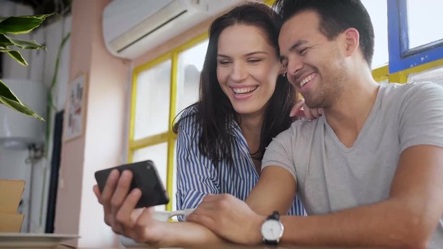 Happy Casual lovely couple emotional reacting, while looking photos in Instagram blogger in cozy loft, watching online stream video on smart phone device, using new application, spending free time