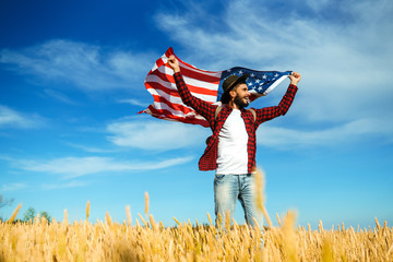 4th of July. Fourth of July. American with the national flag. American Flag. Independence Day. Patriotic holiday. The man is wearing a hat, a backpack, a shirt and jeans. Beautiful sunset light. 