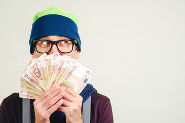 Happy hipster man holding money cash, on white background with copy space. Funny man in glasses holding euro bills, looking aside. Man covered his face by bunch of money