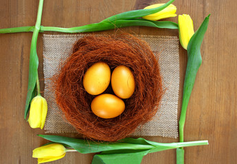 Jajka barwione kurkumą otoczone żółtymi tulipanami i brązowym sizalem