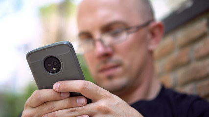 Only Phone in Focus - Late 20s Caucasian Man Texting Using Modern Smartphone With Dual Camera 