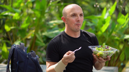 Happy Smiling Young Man Eating Healthy Salad in Park