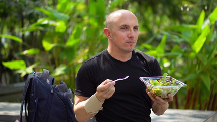 Happy Smiling Young Man Eating Healthy Salad in Park