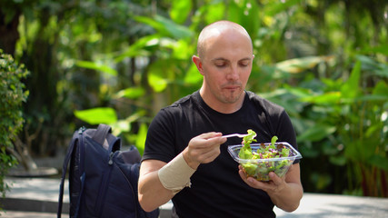 Happy Smiling Young Man Eating Healthy Salad in Park