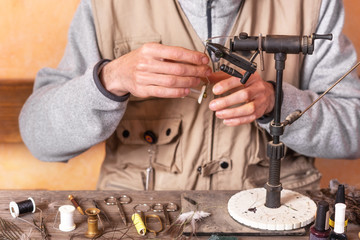 Man making trout flies. Fly tying equipment and material for fly fishing preparation .