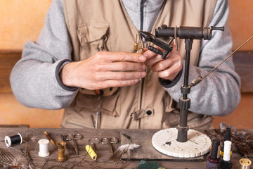 Man making trout flies. Fly tying equipment and material for fly fishing preparation .