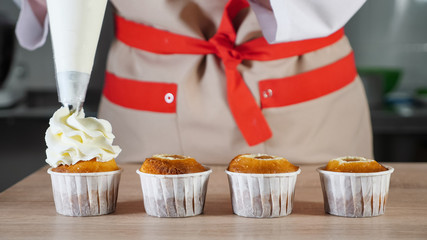 Pastry chef decorates cupcakes in paper cups white cream with pastry bag. Hands close-up. front view