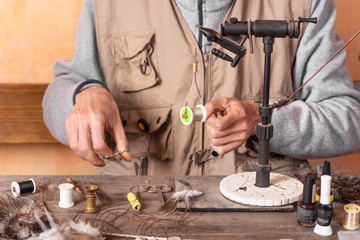 Man making trout flies. Fly tying equipment and material for fly fishing preparation .