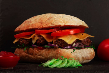 Closeup of delicious fresh homemade burger with lettuce, cheese, onions and tomatoes on dark background