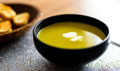 Green broccoli & spinach vegetable soup in black plate on wooden table. Modern kitchen, cooking & healthy food concept. 