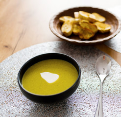 Green broccoli & spinach vegetable soup in black plate on wooden table. Modern kitchen, cooking & healthy food concept. 