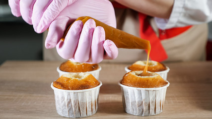 Pastry chef fills muffins in paper cups caramel filling with pastry bag, close-up.