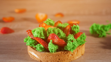 Mini cake with strawberry slices and cream on biscuit pouring with powdered sugar on the table, sunlight