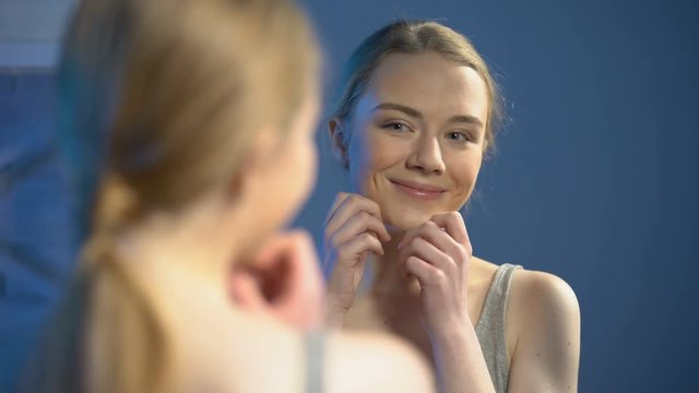 Happy young woman looking at mirror reflection, satisfied with skin treatment