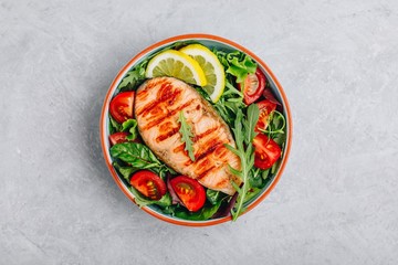 Grilled salmon steak with fresh green arugula salad and tomatoes