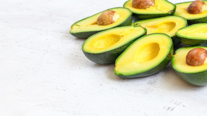 Halved avocados fruits with green yellow pulp, some brown seeds visible on white working board - empty space for text left side