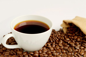 One cup of black coffee with the pile of roasted coffee beans scattered from burlap bag on white background 
