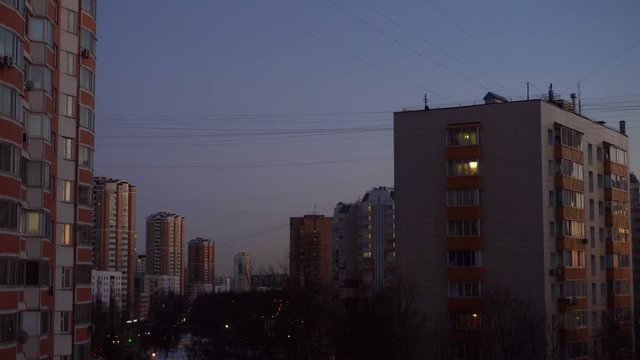 Time Lapse. Sunset. Multi-storey buildings, wires stretched from roof to roof, heavy traffic on the road. Trees without foliage. Early spring. The lights come on in the windows. Ultra HD stock footage