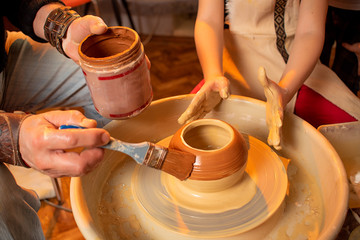 The hands of the potter and the hands of the child work with clay on a special machine. Clay products. Pottery