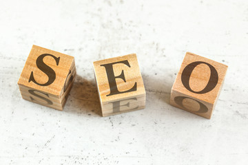 Three wooden cubes with letters SEO stands for Search Engine Optimization on white board.
