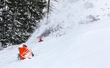 Artificial snow making cannon spraying ice crystals over ski piste, trees in background