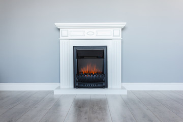 White wooden decorative electric fireplace with a beautiful burning flame. Interior photo on gray...