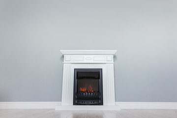 White wooden decorative electric fireplace with a beautiful burning flame. Interior photo on gray...
