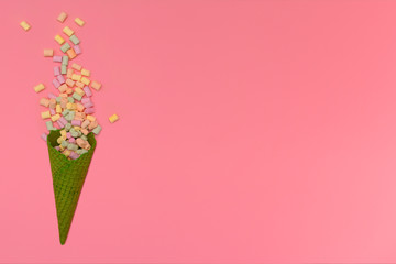 Green waffle ice cream cone. The lie about multi-colored marshmallows isolated on a pink background. Congratulations, celebration concept. Top view. Copy space.