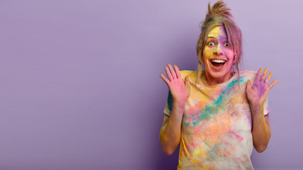 People, emotions and holidays concept. Overemotive happy European woman raises palms from happiness, cant stop positive feelings, being impressed by Holi Festival of Colors celebration abroad