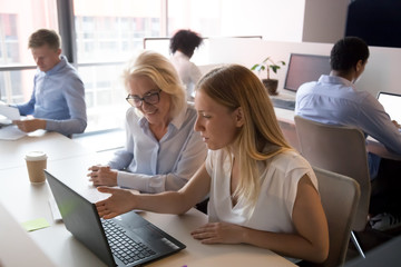 Young saleswoman mentor consulting old client employee pointing at laptop