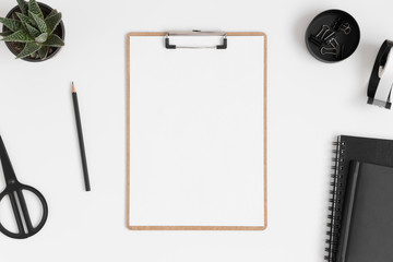 Top view of a wooden clipboard mockup with a succulent plant and workspace accessories on a white table.