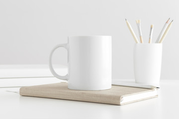 Mug mockup with workspace accessories on a white table.