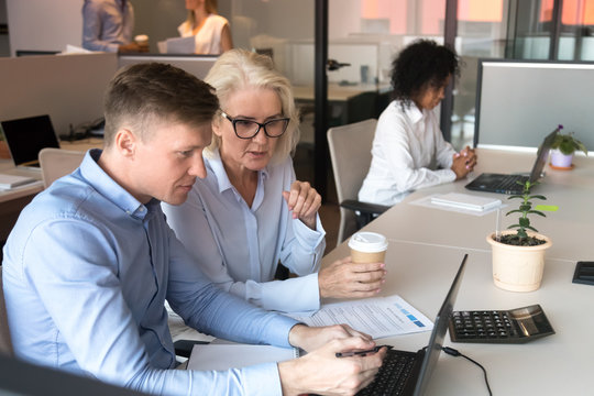 Middle aged colleagues designers discussing project looking at laptop