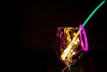 Blue and green glow stick on a wine glass with new year celebration with colorful light relection aginst the dark background party photography