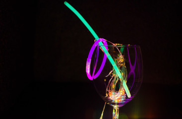 Blue and green glow stick on a wine glass with colorful light relection aginst the dark background...