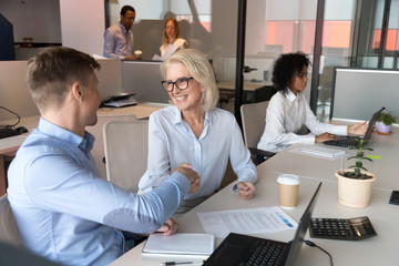 Happy designers colleagues old manager and employee handshake at workplace