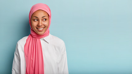 Headshot of beautiful dark skinned female of Arabian appearance, looks aside gladfully, wears...