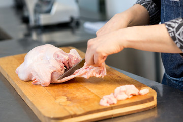 Obraz na płótnie Canvas A person cuts raw chicken. Cook's hand with a knife close-up on the background of the kitchen.