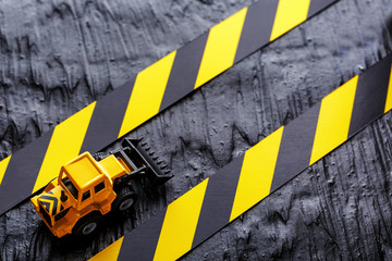 Toy excavator yellow on a black textural background. Tape fencing black yellow against the background of the CONCEPT