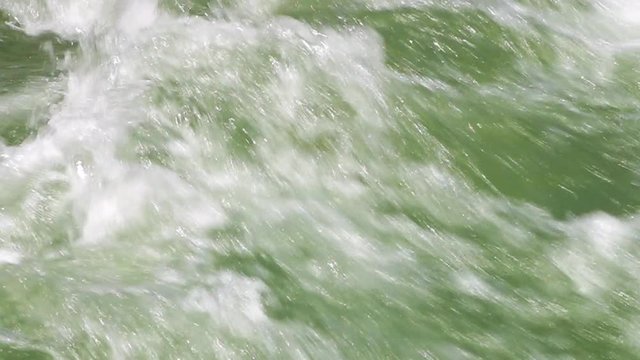 A steady, extreme close up shot of foamy, green, semi clear water heavily falling downwards.